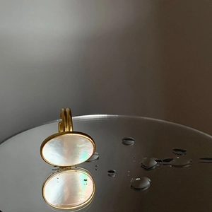 Detailed view of an oval white mother-of-pearl gold ring on black mirror with water drops