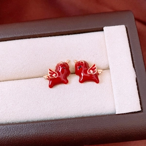 Macro detail of red enamel horse stud earrings with 18k gold plating on beige velvet