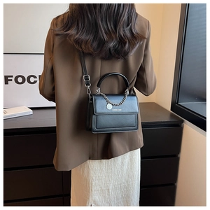 Rear view of a model wearing a black square crossbody bag with a silver chain and pendant