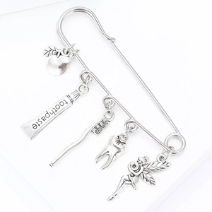 Detailed close-up of a silver brooch pin with dental-themed charms on white background