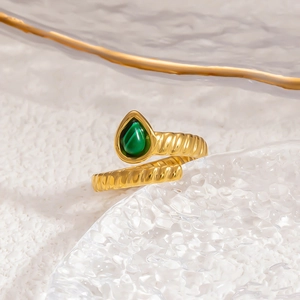 Macro shot of 18k gold snake ring with green stone on a textured glass plate