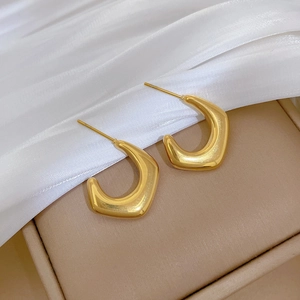 Detailed close-up of a pair of chunky gold C-shaped hoop earrings on white silk fabric