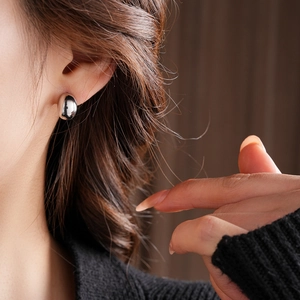 Close-up shot of silver bean-shaped stud earrings worn by a model in soft lighting