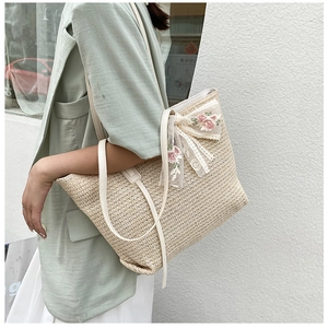 Detail of summer straw tote bag featuring pink floral embroidery and lace bow accent