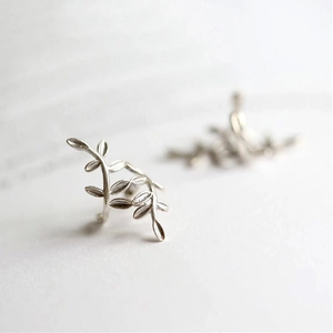 Macro detail of silver leaf shaped non-pierced U-shaped ear cuffs on a clean white surface