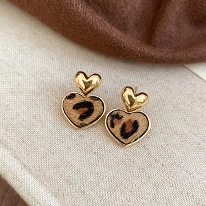 Detail of heart-shaped leopard print earrings with gold metal frame on beige fabric