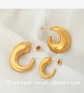 Detail of chunky 18K gold-plated C-shaped hollow earrings on soft fabric