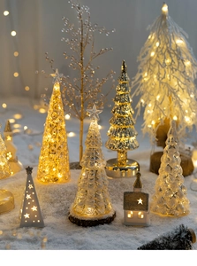 Close-up of glowing LED glass Christmas tree and cottage with warm festive lighting
