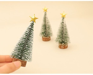 Close-up of mini snow-frosted Christmas trees with golden star and wooden base