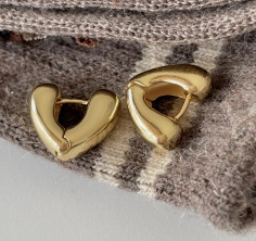 Close-up of heart-shaped gold hoop earrings on a soft grey textured knit fabric