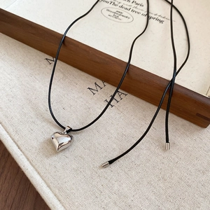 Detailed view of a silver heart pendant necklace on a minimalist black wax cord