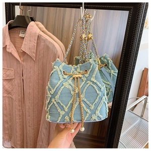 Detail of light blue denim bucket bag with frayed diamond pattern and pearl charm strap