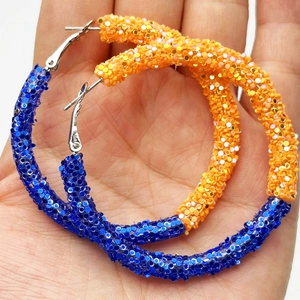 Detail of large blue and orange glitter hoop earrings held in hand for sports events
