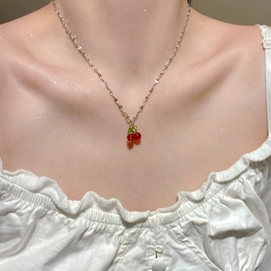 Delicate silver chain necklace with red cherry pendant worn by a model in white top