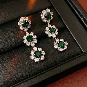 Detailed macro view of silver sunflower earrings with green gemstones in a black box