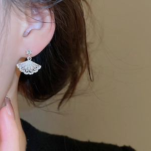 Close-up of silver fan-shaped earrings with zircons worn on a model's ear