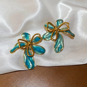 Dettaglio di orecchini a fiocco oro vintage con smalto blu su seta bianca di lusso