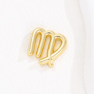 Macro shot of polished gold-plated Virgo zodiac sign pendant on white textured background