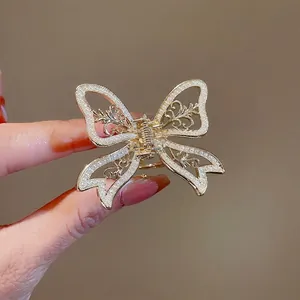 Elegant gold hollow butterfly hair claw clip with pearls shown in hand on warm background