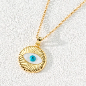 Macro detail of gold evil eye pendant with blue zircon center and textured radiating patterns