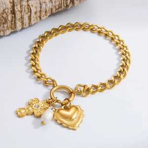 Detail of gold curb chain bracelet with cross, heart charms and pearl on stone decor