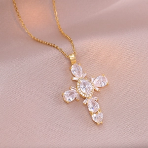 Detail view of a gold cross pendant with cubic zirconia on elegant pink silk fabric