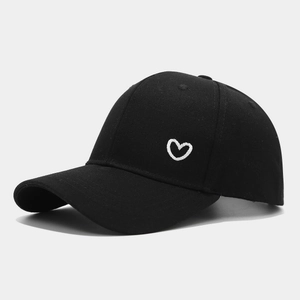 Close-up of white heart embroidery on a black cotton baseball cap with twill texture