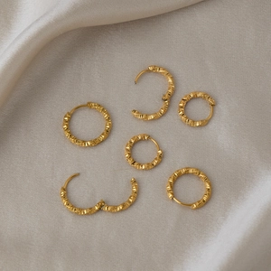 Close-up of gold twisted textured hoop earrings on a beige silk background