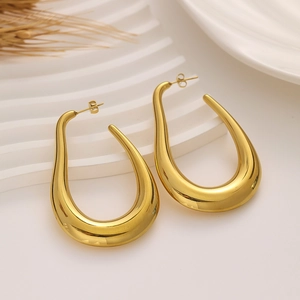 Detailed view of chunky gold drop earrings with a polished mirror finish on white tray