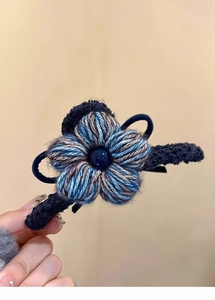 Détail de la pince à cheveux fleur en laine bleue et marron tricotée à la main avec perle