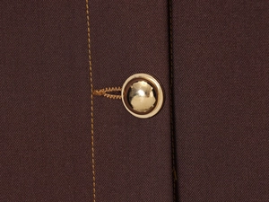 Macro view of dark brown twill fabric with gold dome button and contrast stitching detail