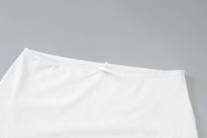 Detail of white floral lace fabric with a small bow accent on a slim fit garment