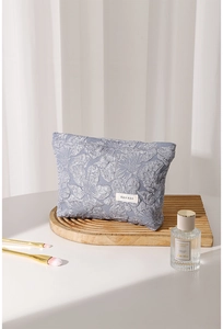 Textured blue canvas cosmetic bag on a wooden tray with brushes and perfume
