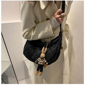 Close-up of black quilted crescent bag with a cute rabbit plush charm on a beige coat