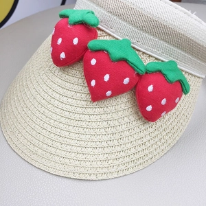 Detailed close-up of a kids' straw sun hat featuring cute 3D plush strawberry accents