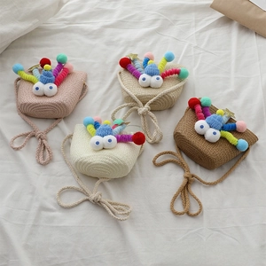 Detail view of colorful woven straw bags for girls featuring fun monster faces and pom-poms