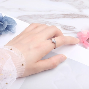 Elegant heart-shaped silver ring on finger with white marble and floral background