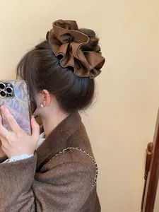 Detailed view of an oversized brown satin scrunchie styled in a low bun on a model