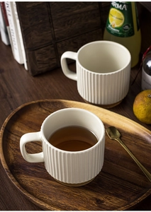 Detail of beige ceramic mugs with vertical ribbed texture on a wooden serving tray