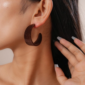 Close-up of a model wearing dark brown velvet C-shape earrings with a vintage texture