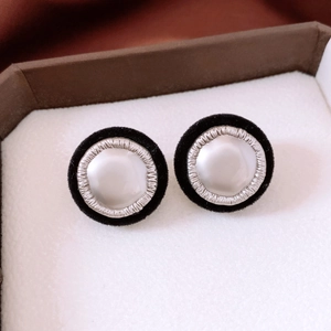 Close-up of retro black flocked earrings with a glossy white pearl center on soft padding