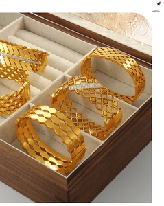 Detailed view of layered geometric hollow gold bangles with cubic zirconia on a wooden tray