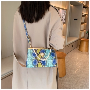 Détail du sac bandoulière serpent sarcelle avec chaîne en perles porté par un mannequin