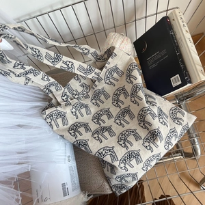 Detail view of canvas tote bag with black animal embroidery in minimalist shopping setting