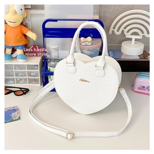 Détail du sac blanc en forme de cœur avec motif crocodile et logo en métal doré