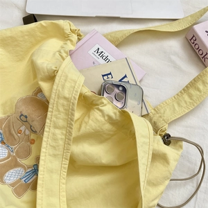 Detail of light yellow drawstring canvas tote bag featuring cute cartoon bear embroidery