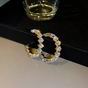 Macro shot of gold C-shaped earrings with square-cut sparkling cubic zirconia stones
