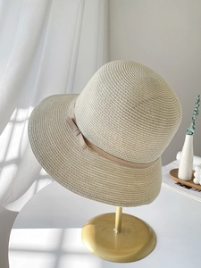 Detail of a beige woven straw hat with a delicate bow ribbon and fine sunshade texture