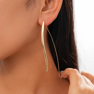 Close-up of a model wearing a long gold metal teardrop hook earring in a modern style