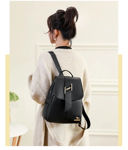 Close-up of black textured leather backpack featuring gold H-buckle on a female model